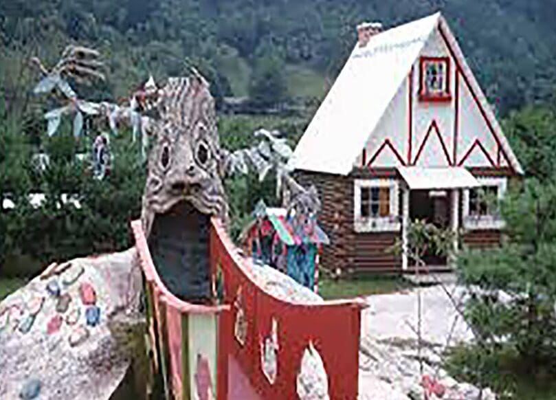 A whimsical wooden dragon sculpture with an open mouth in a village setting.