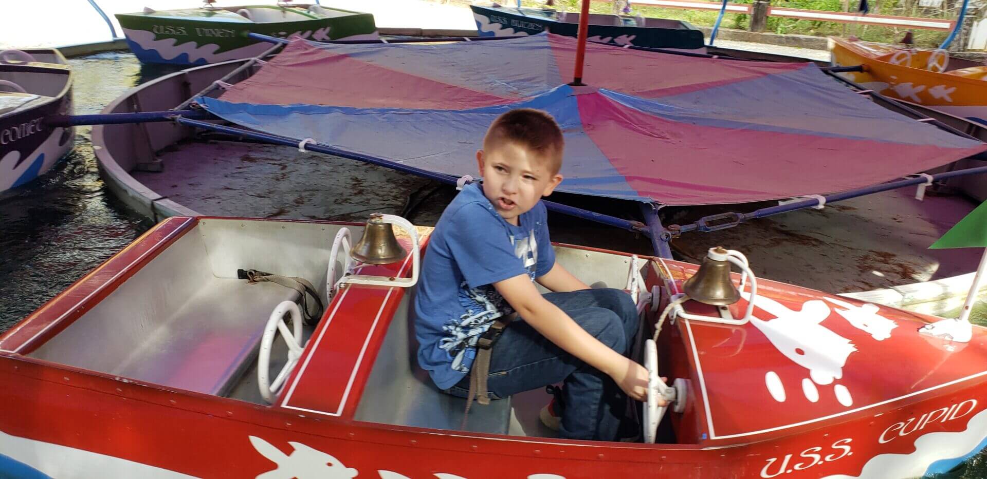 Boy sitting in a small amusement ride boat holding a trophy.