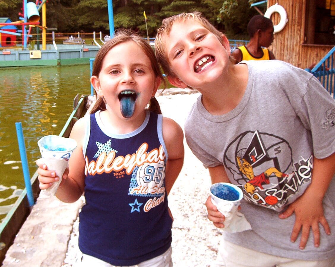 Two kids happily eating blue ice cream outdoors.