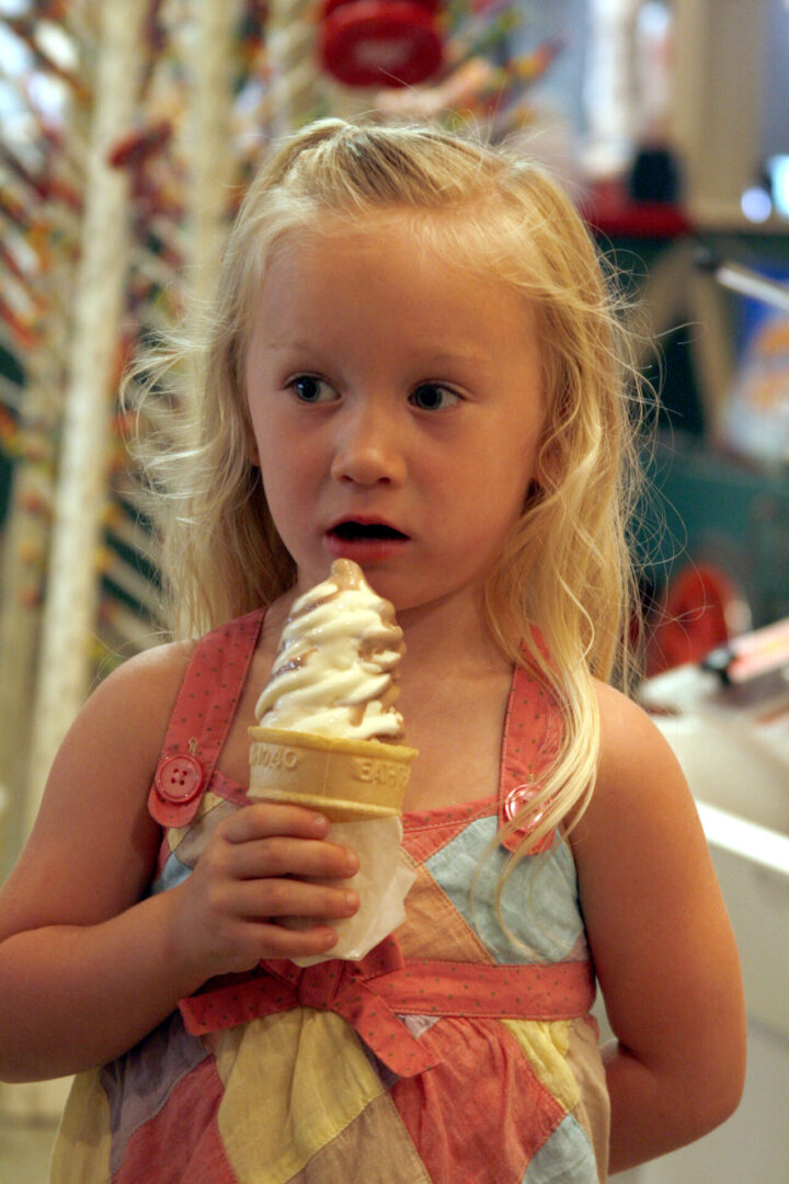 Young girl enjoying a soft serve ice cream cone indoors.