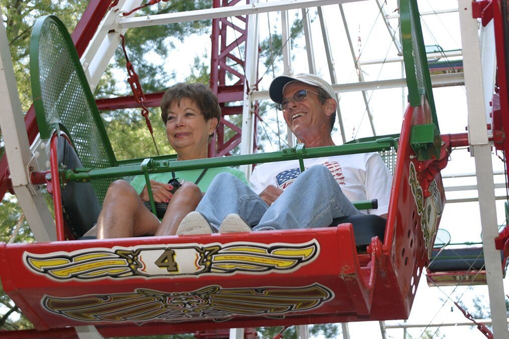Two elderly people sitting in a red amusement park ride basket.