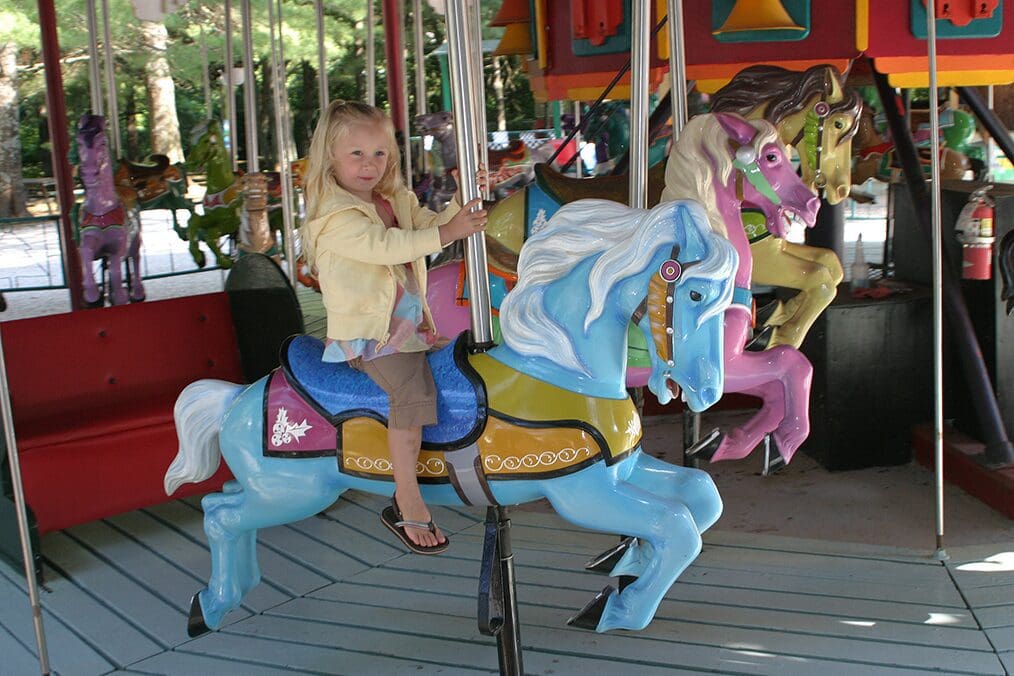 A young girl happily rides a blue carousel horse.